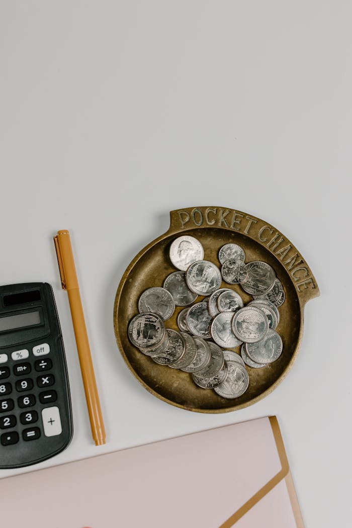 contact-img Top-down view of coins, calculator, and pen on a white surface, ideal for finance concept.